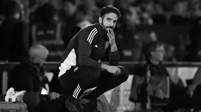 A black and white image of Ruben Amorim hunched on the touchline