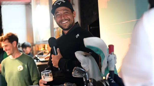 Xander Schauffele talking into a microphone while holding a pint of beer