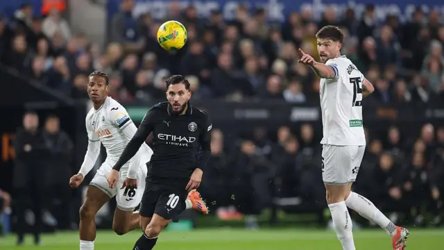 One Manchester City and one Swansea player chasing the ball with one Swansea player standing behind them