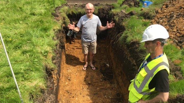 John, in shorts, inspects the grave