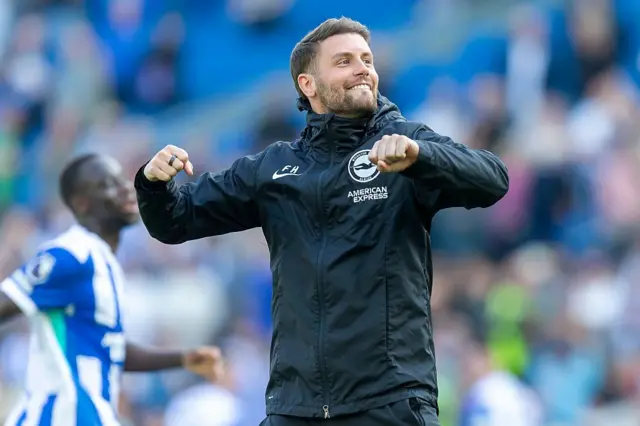 Fabian Hurzeler celebrates. He is wearing a black coat with a Brighton & Hove Albion football team logo on the right chest. 