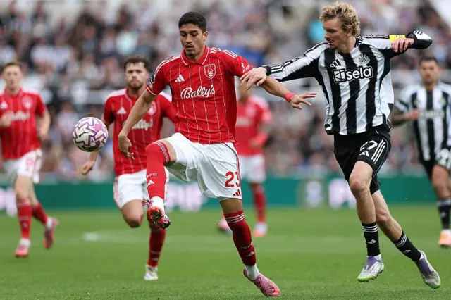 Jair Cunha shielding the ball from Newcastle's Nick Woltemade, with Nottingham Forest and Newcastle players out of focus in the background