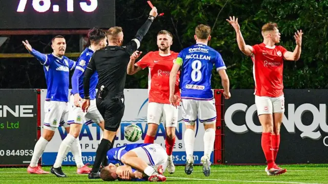 Referee Chris Morrison gives a red card to Leroy Millar
