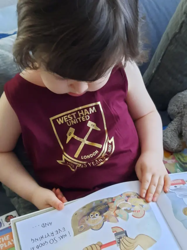 A small girl wears a West Ham dress while reading a book
