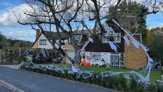 A house decorated for Halloween, there are lots of cobwebs and hanging ghosts as well as inflatable pumpkins outside the front door.