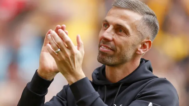 Gary O'Neil, wearing a black Wolves training top, looks up and applauds. His hands are raised near his head and he is smiling