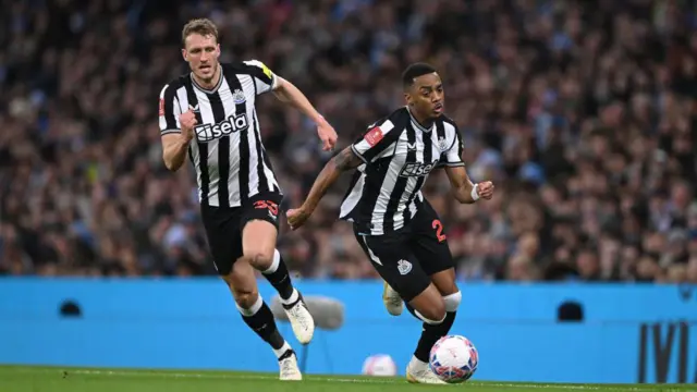 Newcastle player Joe Willock in action watched by Dan Burn during the Emirates FA Cup Quarter Final match between Manchester City and Newcastle United at Etihad Stadium