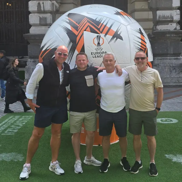 A group of four men posing in front of a large Europa League football