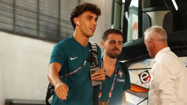 Joao Felix pictured getting off a coach while on international duty with Portugal. He is smiling and earing headphones, with international team-mate Bernardo Silva of Manchester City just behind him.