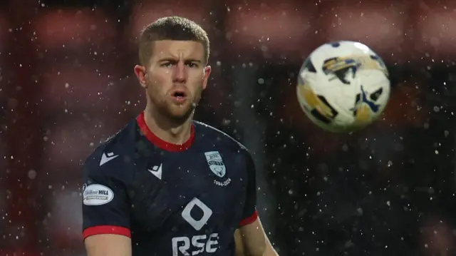 Ryan Leak in action for Ross County. He is wearing a dark blue shirt and is watching the ball move away from him after sending a long pass forward.