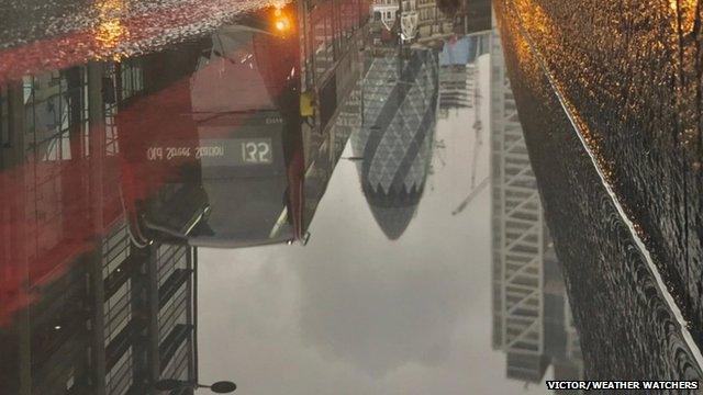 A red bus is reflected in a puddle