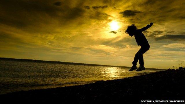 A boy in mid jump on a beach, and he is silhouetted in the sunset