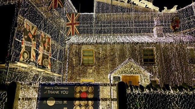 Richard Iles' house completely covered in white string lights. A sign attached to a gate says Merry Christmas and a thank you message to veterans. Union Jack flags are also hung from his home.