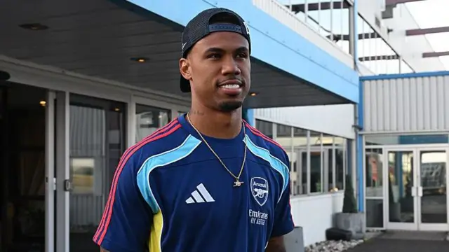Gabriel in a blue Arsenal training top and cap pointing backwards