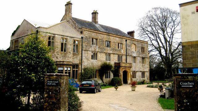 Hooke Court, seen in 2009. The main house is on three floors and has an ornate arched porch surrounding the front doorway. In the foreground a gravelled driveway leads to the property where two cars are parked.