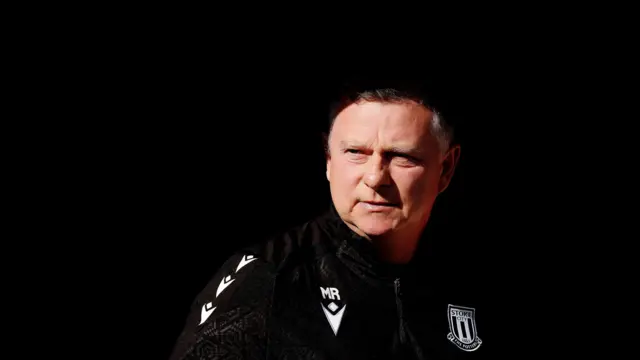 Close up of Stoke City manager Mark Robins in his black club tracktop looking out into the daylight from the dugout