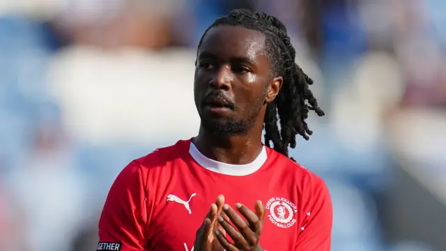 Dion Rankine clapping his hands while walking on the pitch. He is wearing a red Crewe Alexandra shirt