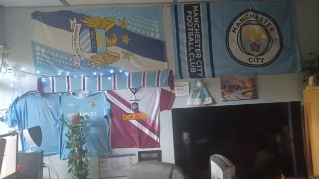 A picture of a wall covered in Man City memorabilia including past shirts and two flags