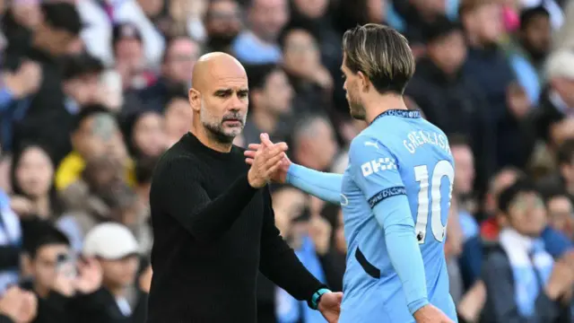 Manchester City's Spanish manager Pep Guardiola (L) hakes hands with Manchester City's English midfielder #10 Jack Grealish (R)