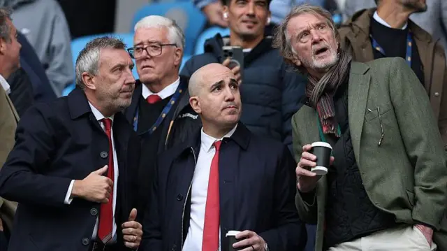 Jason Wilcox, Omar Berrada and Sir Jim Ratcliffe talking to each other in the stands at a match