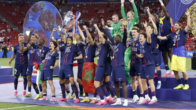 Paris St-Germain players in blue kits celebrate while lifting the Champions League trophy
