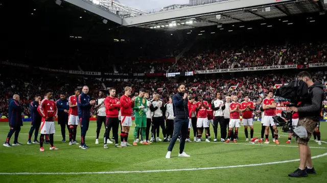 Ruben Amorim stands on the pitch in front of his Manchester United players speaking to the Old Trafford crowd through a microphone