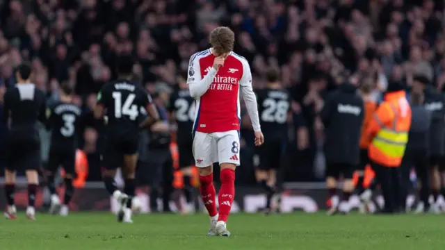 Martin Odegaard looks down as West Ham players celebrate in the background