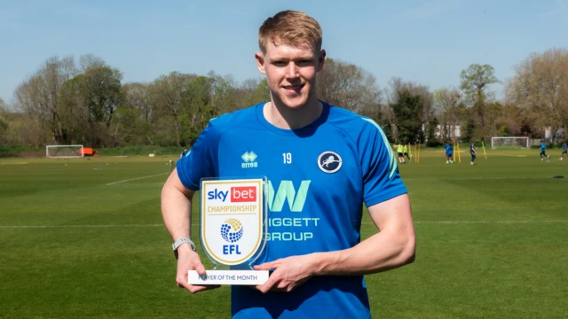 Josh Coburn in a blue Millwall training shirt holding the player of the month trophy