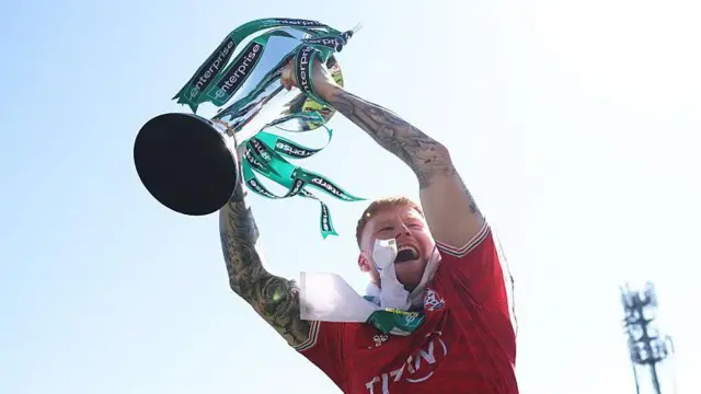 Josh Stones hoists the National League trophy in the air as he celebrates winning the title and promotion to the EFL with York City after their dramatic 1-1 draw with Rochdale in April.