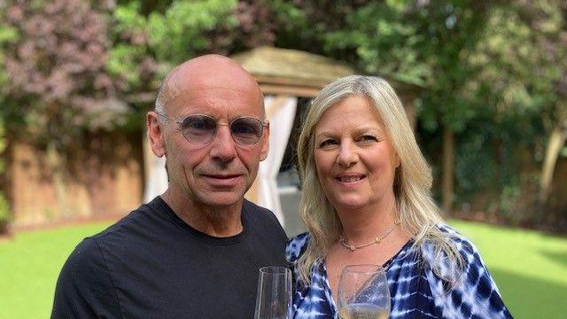 Adam and Jo Hill stood together holding champagne glasses. Their garden is ion the background.