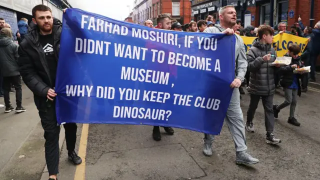 A general view as fans of Everton, holding a banner which reads 'Farhad Moshiri, If You Didnt Want To Become A Museum, Why Did You Keep The Club Dinosaur?'