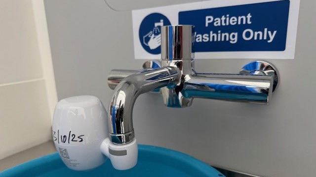 A tap on Wexham Park Hospital's intensive care unit sits above a bright blue plastic bowl. The tap has a white plastic sleeve over it to stop the water from spraying everywhere. The bowl itself sits on a stainless shelf with no drain or pipes in sight.