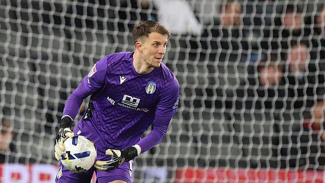 Colchester United goalkeeper Matt Macey in a purple shirt prepares to throw the ball