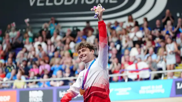 Matthew Robertson holds up his mascot with his gold medal around his neck at the Sir Chris Hoy Velodrome