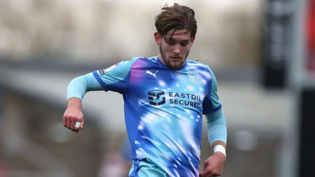 A photo of Dom Ballard, wearing a blue and purple Leyton Orient kit, playing for the O's against Northampton Town in February