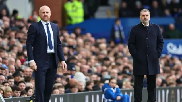 Sean Dyche, wearing a dark suit, and Ange Postecoglou, wearing a dark coat, stand side by side on the touchline during a match
