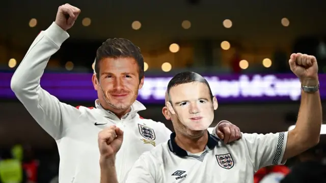 England supporters wear masks of former football players David Beckham (L) and Wayne Rooney