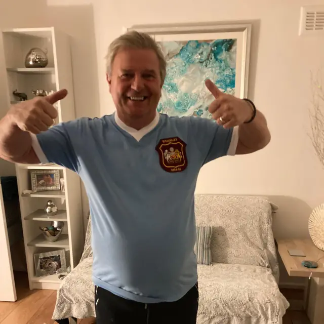 A man in a vintage Manchester City top poses with his thumbs up