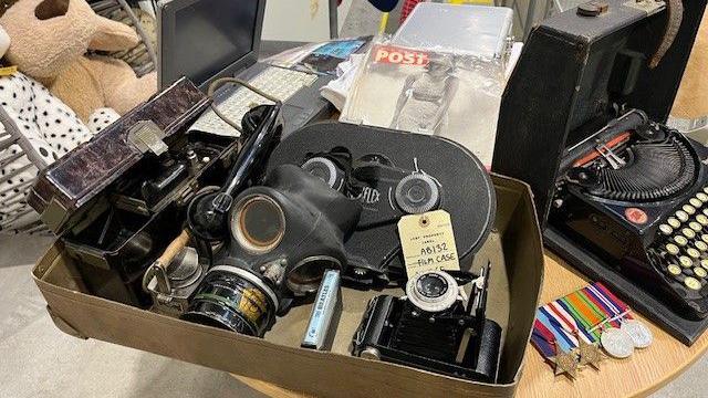 A gas mask, old cameras, old type writer and war medals sit on a desk