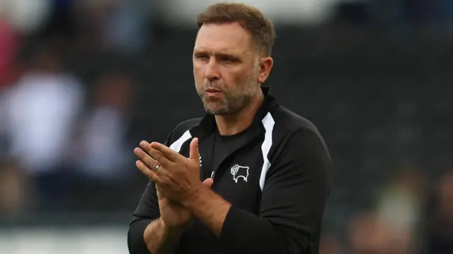 John Eustace, wearing a black Derby County tracksuit top, claps the fans after the 2-2 draw with Cardiff at Pride Park
