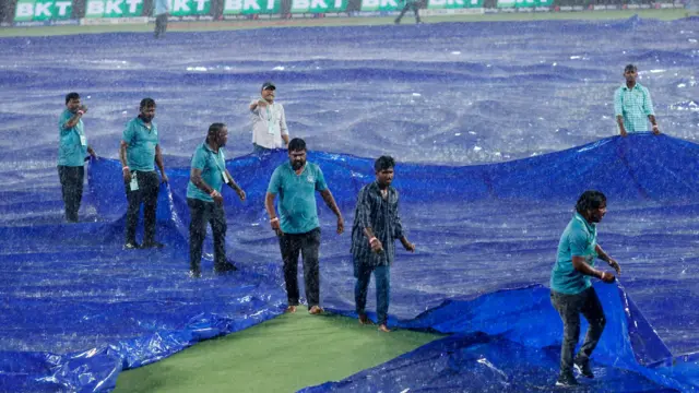 Groundstaff attempt to cover playing area in rain