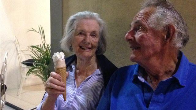 Jocelyn and Mark Tress sitting beside each other as she holds up an ice cream to the camera. He is looking away and up from the camera.