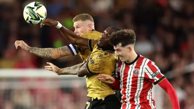 James McClean and Sebastian Revan of Wrexham battle for a header with Owen Hampson of Sheffield United during the Carabao Cup first round