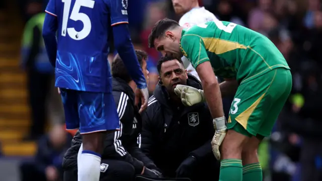 Emiliano Martinez of Aston Villa receives medical treatment for an injury before being substituted during the Premier League match between Chelsea FC and Aston Villa FC at Stamford Bridge