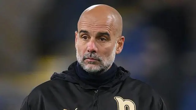 Guardiola in a black jacket with gold details watching on from the sidelines.