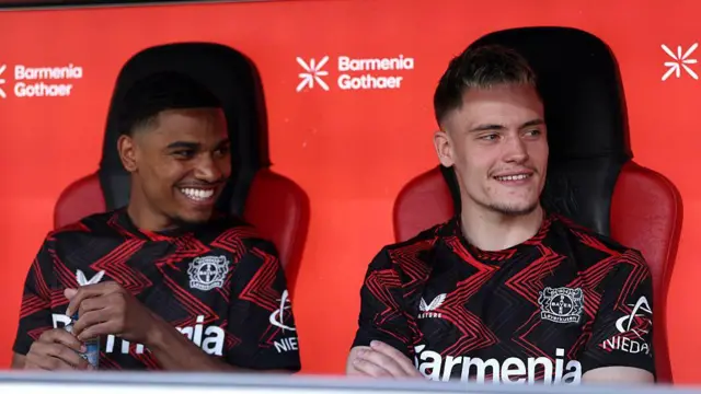 Amine Adli and Florian Wirtz look on while sitting on the substitutes bench