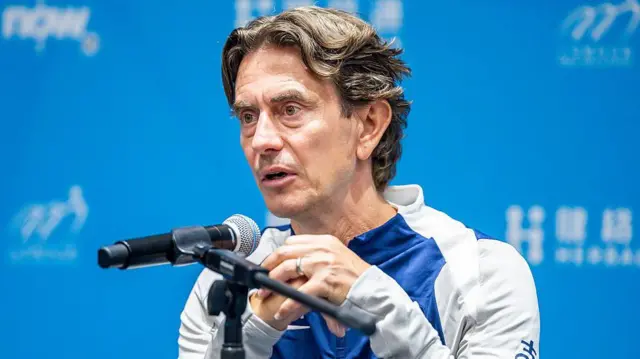 Thomas Frank sits in front of a blue background with a microphone before him