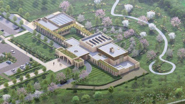 Artist's aerial impression  of the crematorium, showing a central mainly single storey building in light stone, with a chimney above one section. An entrance is visible, opening out onto a paved square area. There are tree-lined pathways surrounding the building.