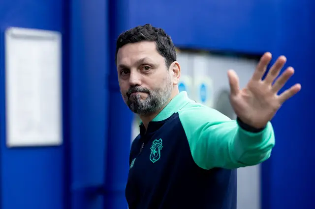 Erol Bulut raises a hand to wave as he walks into a stadium before a game