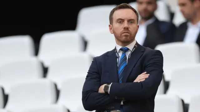 Mike Cave looks on from the stands with his arms folded